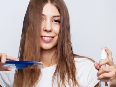 Une femme qui applique du spray protecteur de chaleur sur ses cheveux épais avant lissage